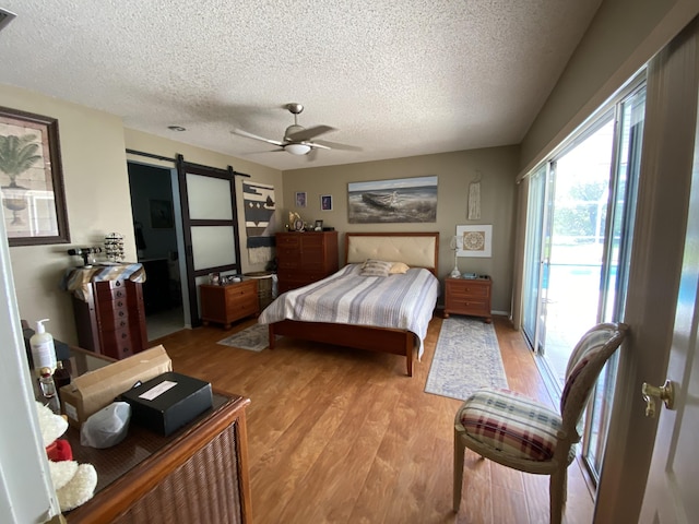 bedroom with light wood-style flooring, a ceiling fan, a textured ceiling, a barn door, and access to exterior