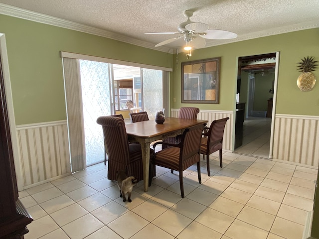 dining space featuring light tile patterned floors, a wainscoted wall, a textured ceiling, and a ceiling fan