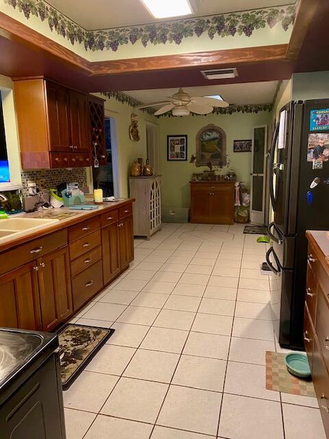 kitchen featuring sink, tasteful backsplash, light tile patterned floors, black refrigerator, and ceiling fan