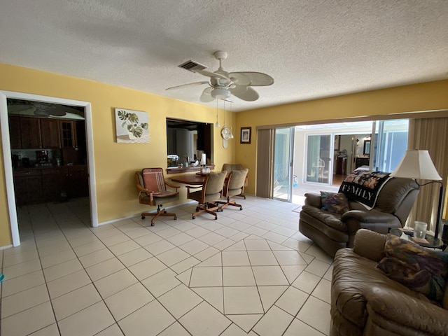 living area featuring light tile patterned floors, a ceiling fan, visible vents, and a textured ceiling