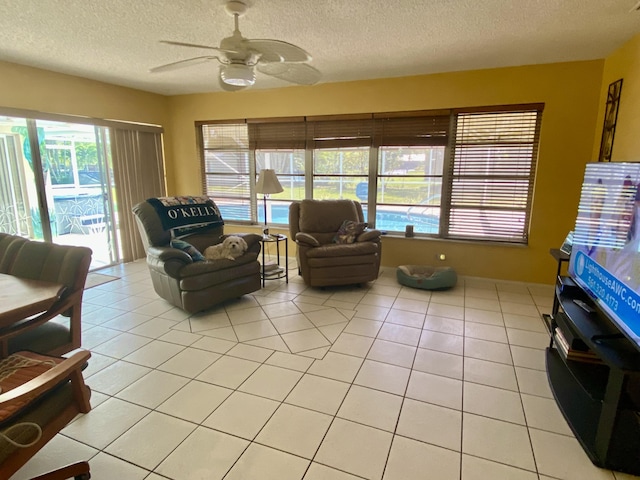 living area with a textured ceiling, light tile patterned floors, and ceiling fan