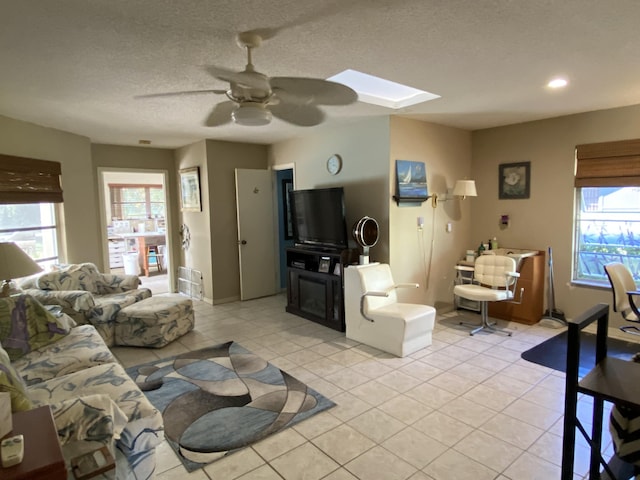 living area featuring a ceiling fan, a textured ceiling, recessed lighting, a skylight, and light tile patterned floors