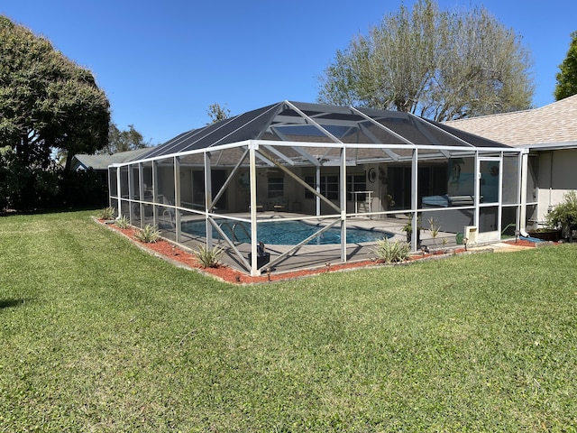 rear view of house featuring glass enclosure, a patio, an outdoor pool, a shingled roof, and a lawn