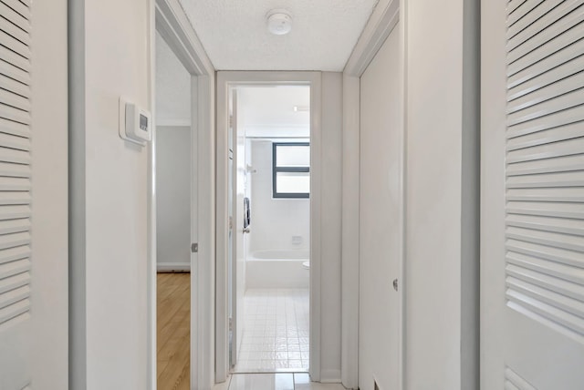 hallway with a textured ceiling and light hardwood / wood-style floors