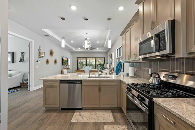 kitchen featuring stainless steel appliances, kitchen peninsula, sink, and a raised ceiling