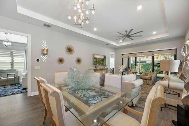 dining room with hardwood / wood-style floors, ceiling fan with notable chandelier, and a raised ceiling