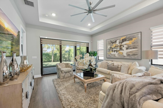 living room featuring ceiling fan, a tray ceiling, and dark hardwood / wood-style flooring