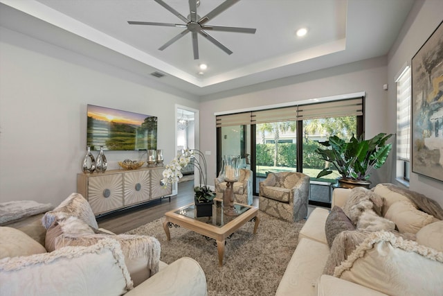 living room featuring wood-type flooring, a raised ceiling, and ceiling fan