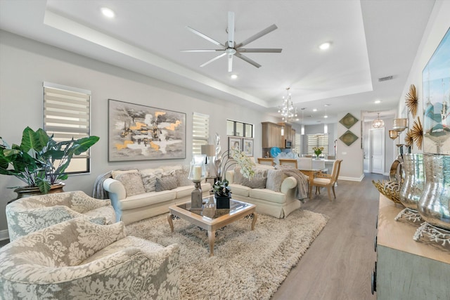 living room featuring ceiling fan, a tray ceiling, and light wood-type flooring