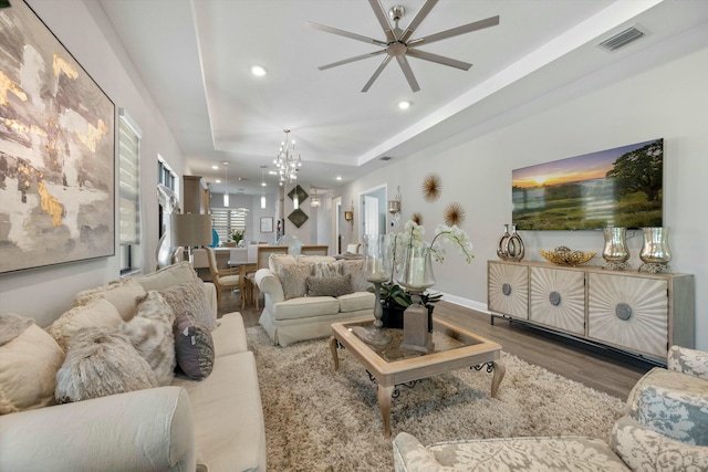 living room with a raised ceiling, ceiling fan with notable chandelier, and hardwood / wood-style floors