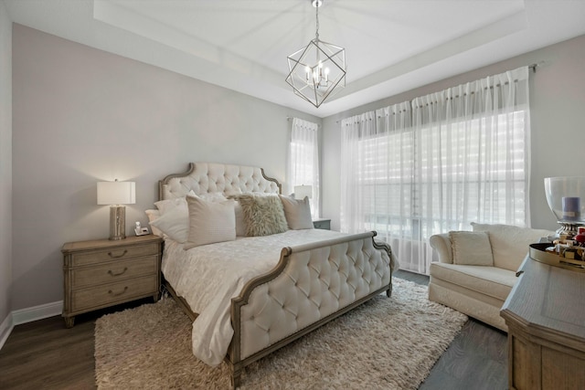 bedroom featuring dark wood-type flooring, a tray ceiling, and a notable chandelier