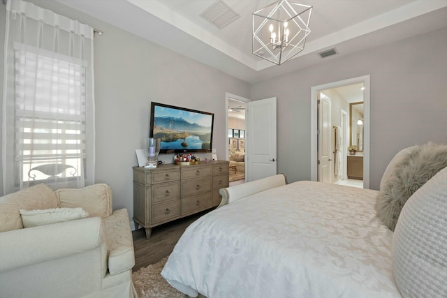 bedroom featuring hardwood / wood-style flooring, connected bathroom, a tray ceiling, and a notable chandelier