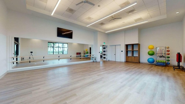 workout area with a high ceiling, a raised ceiling, ceiling fan, and light hardwood / wood-style flooring