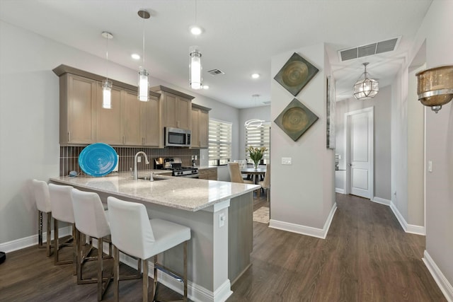 kitchen with sink, light stone counters, hanging light fixtures, appliances with stainless steel finishes, and kitchen peninsula