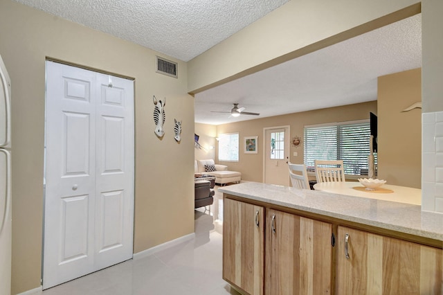 kitchen featuring visible vents, light brown cabinetry, light stone counters, a textured ceiling, and ceiling fan