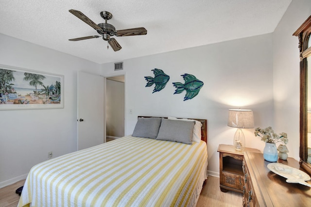 bedroom featuring baseboards, wood finished floors, visible vents, and a textured ceiling