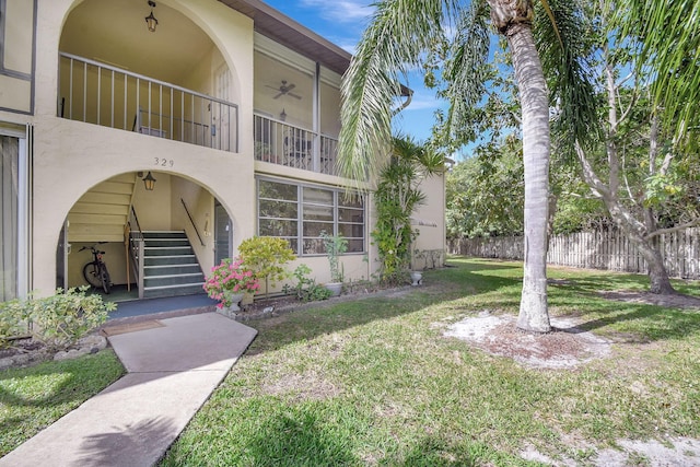 exterior space with stucco siding, a yard, ceiling fan, and fence