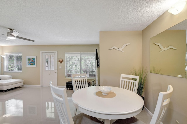 tiled dining room featuring baseboards, a healthy amount of sunlight, a textured ceiling, and a ceiling fan