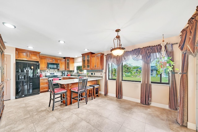 kitchen featuring light tile patterned floors, hanging light fixtures, tasteful backsplash, black appliances, and a kitchen bar