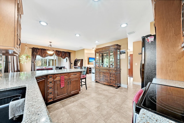 kitchen featuring black fridge, light stone countertops, hanging light fixtures, and range with electric stovetop