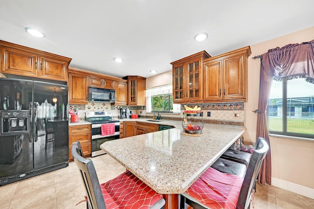 kitchen featuring a kitchen bar, light stone counters, black appliances, light tile patterned floors, and backsplash