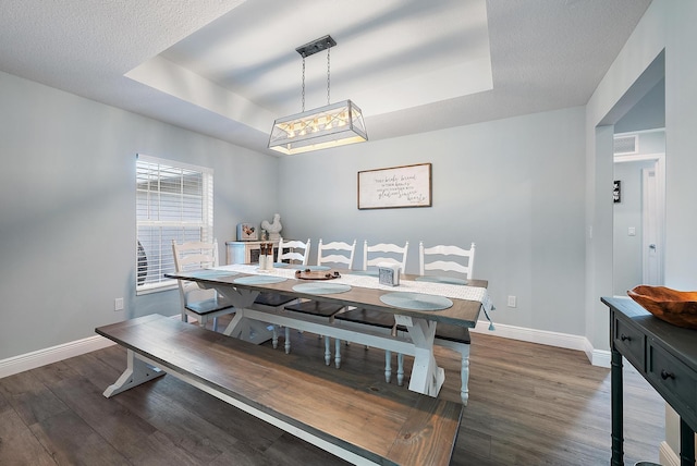 dining area featuring dark wood-type flooring, a textured ceiling, and a tray ceiling