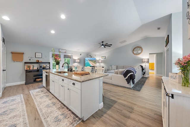 kitchen with sink, white cabinets, stainless steel dishwasher, light stone countertops, and a center island with sink