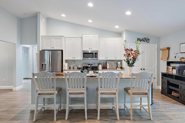 kitchen featuring stainless steel appliances, a kitchen island with sink, white cabinets, and a breakfast bar