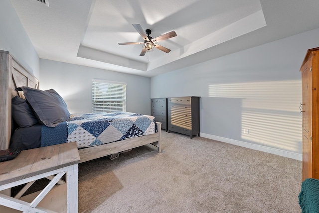 bedroom featuring light carpet, a tray ceiling, and ceiling fan