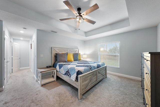 carpeted bedroom with a textured ceiling, ceiling fan, and a tray ceiling