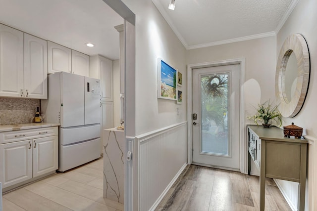 foyer entrance with light wood finished floors, a wainscoted wall, a textured ceiling, and crown molding