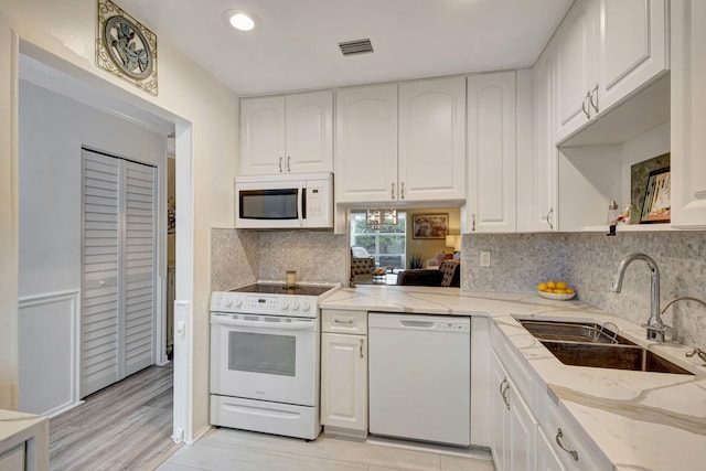 kitchen with visible vents, light stone countertops, white appliances, white cabinetry, and a sink