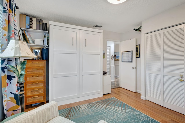 bedroom with visible vents, light wood-type flooring, two closets, and a textured ceiling