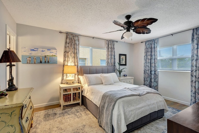 bedroom with light wood-style flooring, a ceiling fan, baseboards, and a textured ceiling