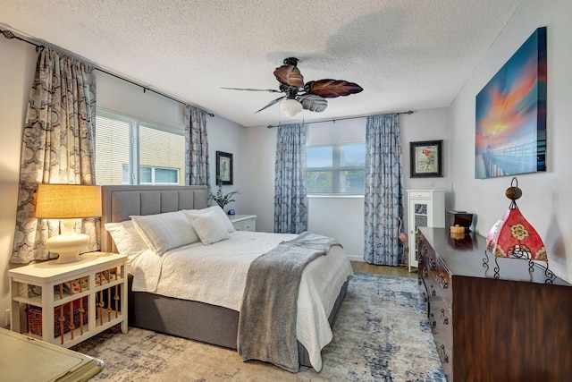 bedroom with ceiling fan, multiple windows, a textured ceiling, and wood finished floors