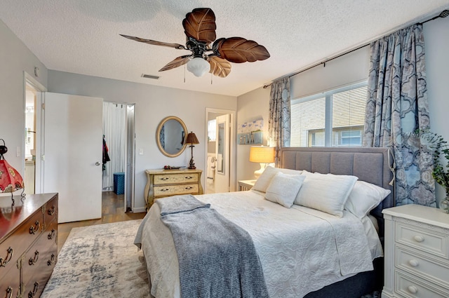 bedroom with a spacious closet, a ceiling fan, visible vents, and a textured ceiling