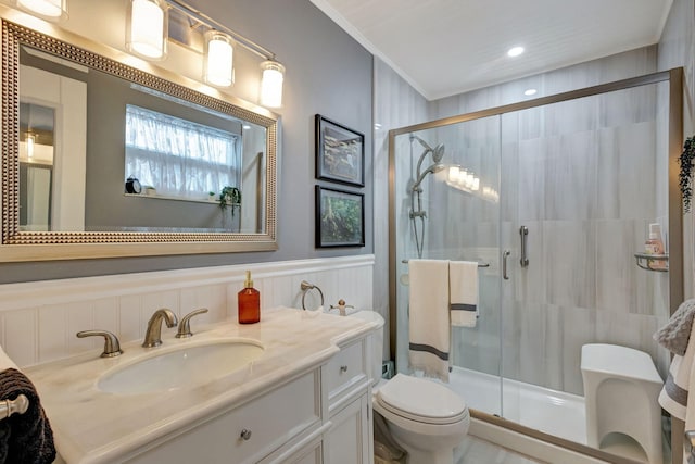 bathroom with crown molding, a wainscoted wall, toilet, a stall shower, and vanity