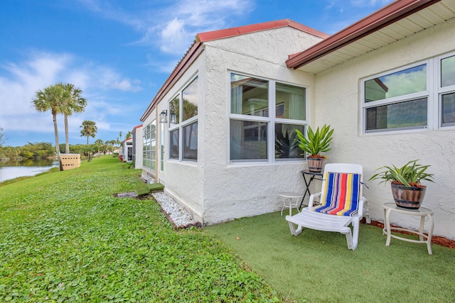 view of home's exterior with stucco siding, a water view, and a lawn