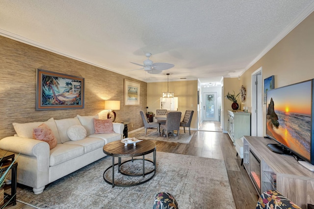 living area featuring wood finished floors, baseboards, ceiling fan, ornamental molding, and a textured ceiling