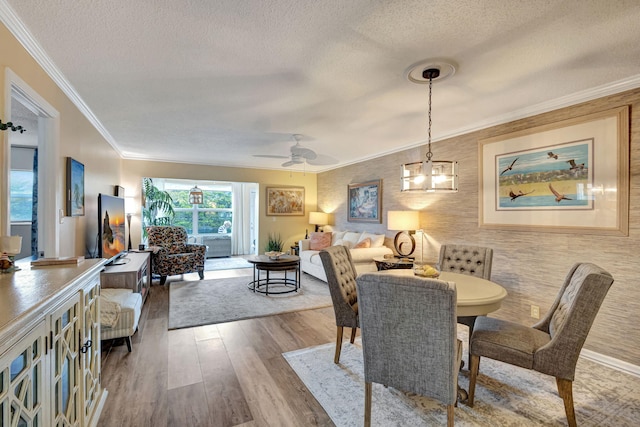 dining area with ceiling fan with notable chandelier, ornamental molding, wood finished floors, and a textured ceiling