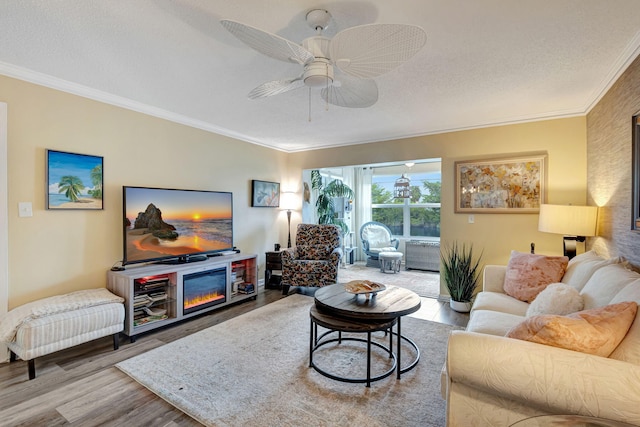 living room featuring wood finished floors, ceiling fan, a textured ceiling, a glass covered fireplace, and crown molding