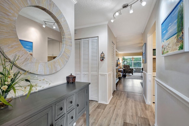 hall with ornamental molding, wainscoting, light wood finished floors, and a textured ceiling