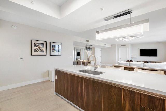 kitchen featuring dark brown cabinets, decorative light fixtures, sink, and light hardwood / wood-style flooring