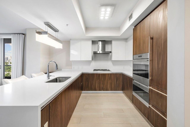 kitchen featuring sink, wall chimney range hood, white cabinets, and kitchen peninsula