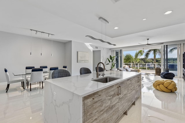 kitchen featuring sink, ceiling fan, a kitchen island with sink, light stone countertops, and decorative light fixtures