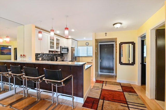 kitchen with a breakfast bar area, kitchen peninsula, pendant lighting, stainless steel appliances, and white cabinets