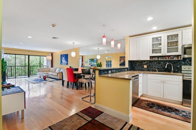 kitchen with appliances with stainless steel finishes, decorative light fixtures, white cabinets, a kitchen bar, and kitchen peninsula