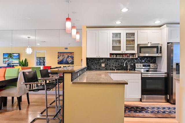 kitchen featuring hanging light fixtures, stainless steel appliances, kitchen peninsula, and a kitchen bar