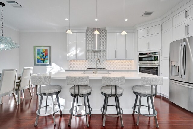 kitchen with sink, white cabinetry, hanging light fixtures, an island with sink, and wall chimney range hood