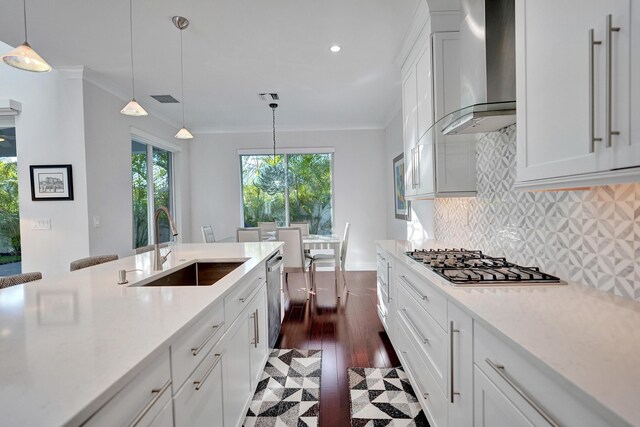 kitchen with wall chimney range hood, white cabinetry, backsplash, a kitchen bar, and decorative light fixtures